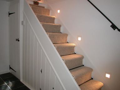 A staircase with carpeted steps and built in storage under the stairs with white panelled doors and black handles at Gun Hill Cottage in Heathfield