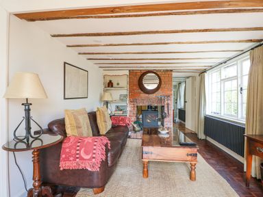 A living room with a leather sofa pillows a wooden coffee table and a brick fireplace at Gun Hill Cottage in Heathfield
