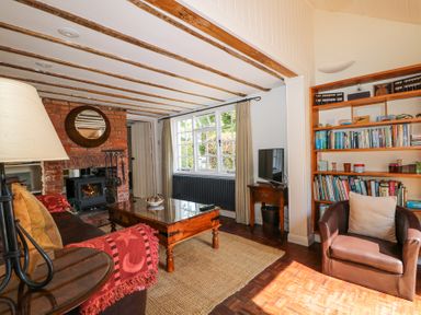 A living room with a brick fireplace wooden coffee table bookshelf and a brown armchair at Gun Hill Cottage in Heathfield