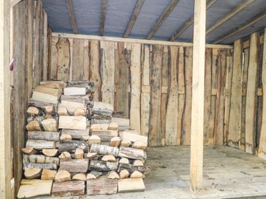 A wooden shed with a stack of cut firewood inside at Gun Hill Cottage in Heathfield