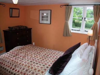 A bedroom with a bed covered with a patterned bedspread next to a window with curtains and a dark wooden dresser at Gun Hill Cottage in Heathfield