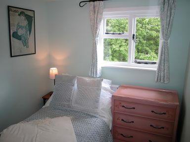 A bedroom with a bed next to a window a pink chest of drawers and a framed Picasso poster on the wall at Gun Hill Cottage in Heathfield