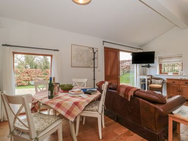 A dining area with a table and chairs next to a living area with a leather sofa and a wall-mounted TV at Russet in Martin