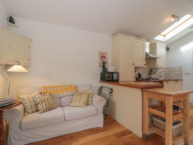 A small living area with a beige sofa and pillows next to a kitchen with cabinets and a wooden floor at Russet in Martin