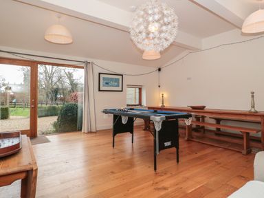 A game room with a pool table wooden benches a long wooden table and glass doors leading to a garden at Russet in Martin