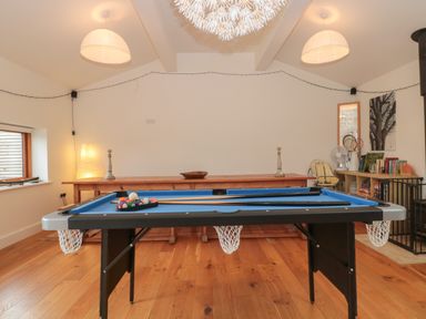 A room with a pool table in the center a wooden table with candlesticks and a bowl against the wall and shelves with books and a fan at Russet in Martin