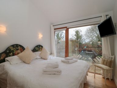 A bedroom with a large bed two pillows folded towels a wall-mounted tv a chair and a glass door leading outside at Russet in Martin
