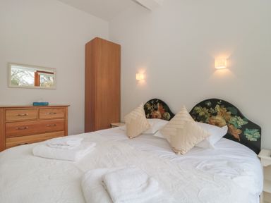 A bedroom with a double bed with floral headboard two pillows towels on the bed a wooden dresser with a mirror and a wardrobe at Russet in Martin