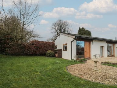 A single story house with white walls and wooden doors next to a gravel pathway and lawn at Russet in Martin