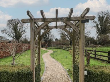 A wooden garden arch over a gravel pathway with grass and trees on either side at Russet in Martin