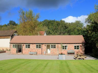A single story brick building with multiple windows a bench picnic table and a grassy lawn at The Old Dairy in Flaxley