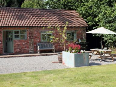 An outdoor area with a brick building bench picnic table umbrella and planter at The Old Dairy in Flaxley