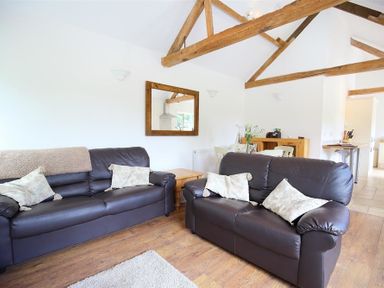 A living room with two brown leather sofas a wooden coffee table and exposed wooden ceiling beams at The Old Dairy in Flaxley