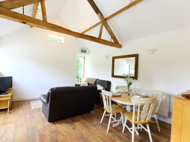 A living room with a wooden dining table with chairs and black sofas at The Old Dairy in Flaxley
