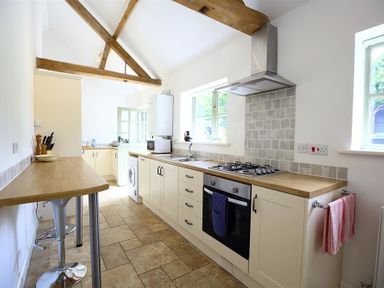 A kitchen with wooden beams a tiled floor gas stove oven microwave and washing machine at The Old Dairy in Flaxley