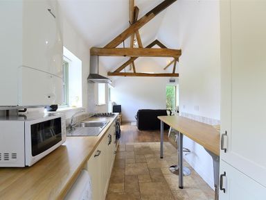 A kitchen with wooden countertops, microwave, sink, stove, and exposed wooden beams at The Old Dairy in Flaxley