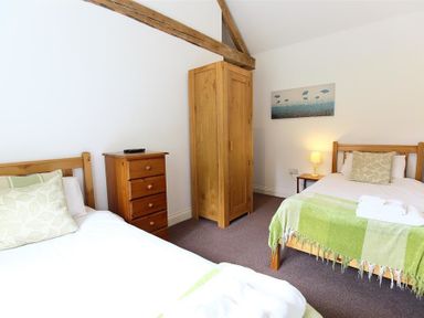 A bedroom with two single beds a wooden wardrobe chest of drawers and a bedside table with a lamp at The Old Dairy in Flaxley