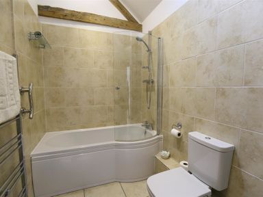 A bathroom with a bathtub shower combination toilet towel rack and beige tiled walls at The Old Dairy in Flaxley