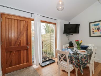 A dining area with wooden door table with floral tablecloth white chairs wall mounted television and a framed picture at Pippin in Martin