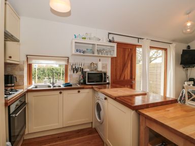 A kitchen with cream cabinets wooden countertops a sink oven microwave knives and a washing machine at Pippin in Martin