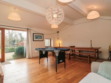 A room with a small pool table a wooden bench table and large glass doors showing outside garden at Pippin in Martin