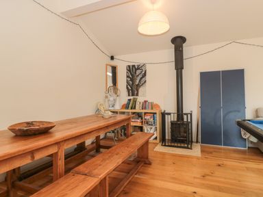 A room with a wooden dining table and bench a small bookshelf with books and board games a black wood stove with a safety gate a blue folded ping pong table and a pool table at Pippin in Martin
