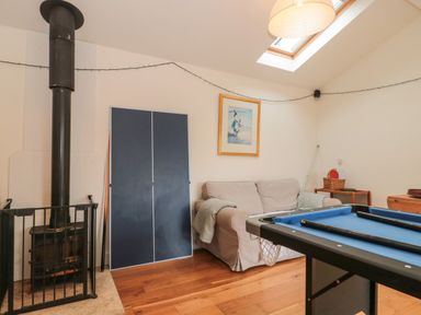 A room with a wood stove, a folded ping pong table, a beige sofa, a pool table with blue felt, a framed painting, and a skylight at Pippin in Martin
