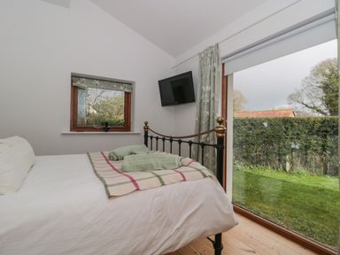 A bedroom with a bed with white linens and a plaid blanket beside a window and a glass door with a view of a garden at Pippin in Martin