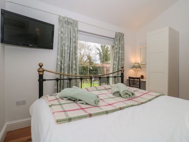 A bedroom with a bed covered with a blanket and towels a wall mounted television curtains a white wardrobe and a desk with a chair and lamp at Pippin in Martin