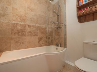A bathroom with a bathtub and shower combo tiled walls and a toilet with a wooden shelf above it at Pippin in Martin