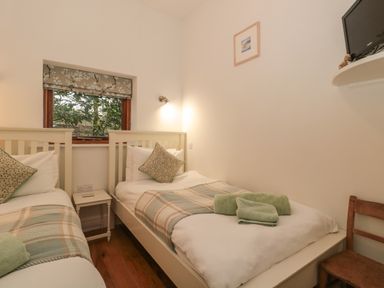 A bedroom with two single beds a small table with a remote a window and a chair at Pippin in Martin