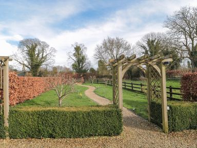 A gravel pathway passing through a wooden garden arch with hedges and trees lining the path at Pippin in Martin