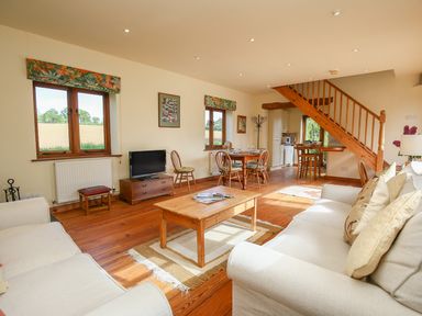 A living room with sofas coffee table dining table and wooden staircase at The Coach House in Lympstone