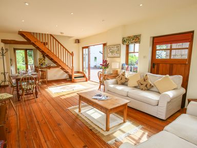 A living room with wooden furniture a sofa with cushions a coffee table and a staircase at The Coach House in Lympstone