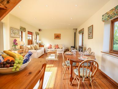 A living room and dining area with wooden furniture and fruit bowl on table at The Coach House in Lympstone