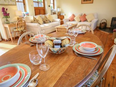 A dining table set with plates glasses and cutlery in a living room with sofas and a wooden floor at The Coach House in Lympstone