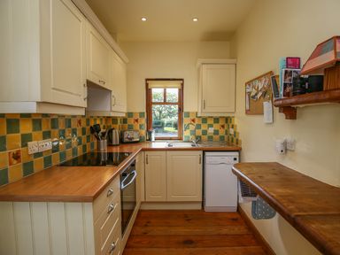 A kitchen with wooden countertops tiled backsplash and cabinets with a window above the sink at The Coach House in Lympstone