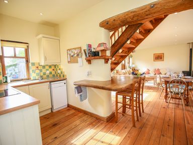 A kitchen and dining area with wooden flooring wooden stairs and a seating area at The Coach House in Lympstone