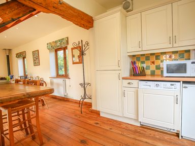 A kitchen and dining area with wooden floor a wooden table chairs white cabinets a microwave and a colorful knife set at The Coach House in Lympstone