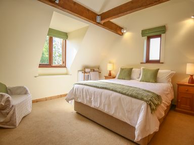 A bedroom with a bed pillows lamps a chair and two windows at The Coach House in Lympstone