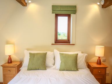 A bedroom with a double bed with white linens green pillows two wooden bedside tables with lamps and a window above the bed at The Coach House in Lympstone