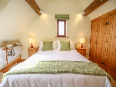 A bedroom with a double bed with green pillows and blanket two wooden nightstands with lamps and a wooden wardrobe at The Coach House in Lympstone