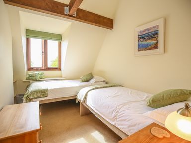 A bedroom with two single beds a wooden chest of drawers a window with green blinds and folded towels at The Coach House in Lympstone