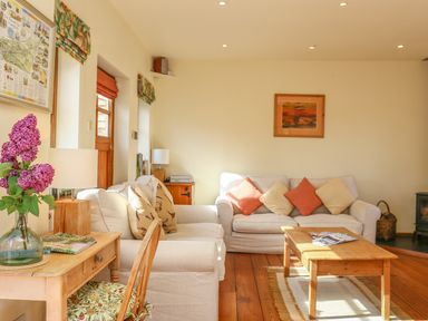 A living room with beige sofas cushions wooden coffee table and a desk with flowers at The Coach House in Lympstone