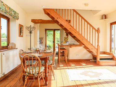 A dining room with a wooden table and chairs set under stairs with a door leading outside at The Coach House in Lympstone