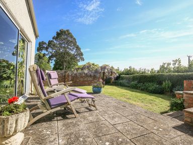 A patio with two wooden lounge chairs with purple cushions and a garden with grass and plants at The Coach House in Lympstone