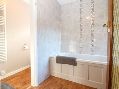 A bathroom with a bathtub and a grey towel hanging on the bathtub at Spring Cottage in Wroxton
