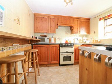 A kitchen with wooden cabinets stools microwave and oven at Spring Cottage in Wroxton