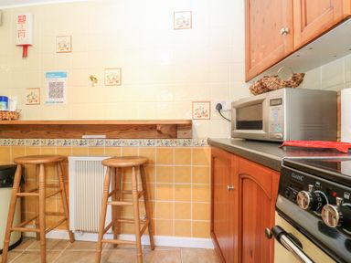 A kitchen area with two wooden stools, a microwave on a countertop, and a stove at Spring Cottage in Wroxton