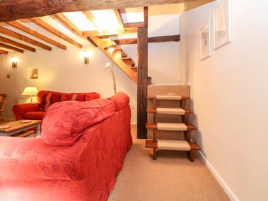 A living room with red sofas wooden beams on ceiling and a small wooden staircase at Spring Cottage in Wroxton